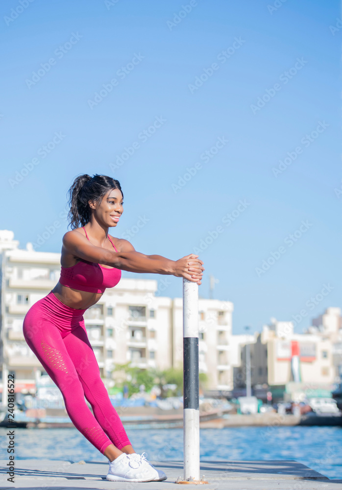 Beautiful tall athletic African American Woman does a stretch pose wearing  a bright pink workout outfit