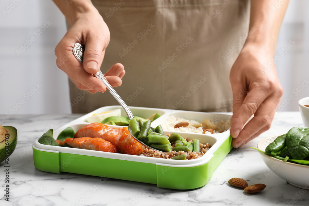 Woman putting natural protein food into container on marble table, closeup Woman putting natural protein food into container on marble table, closeup