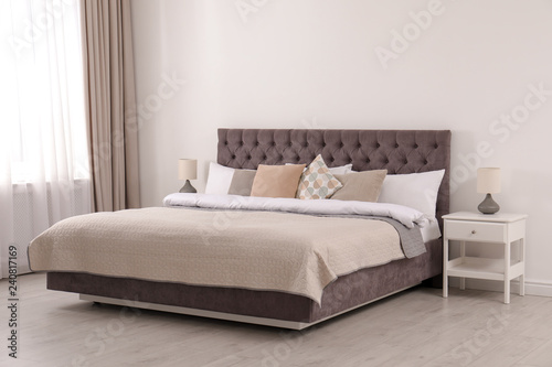 Large comfortable bed near light wall in simple room interior