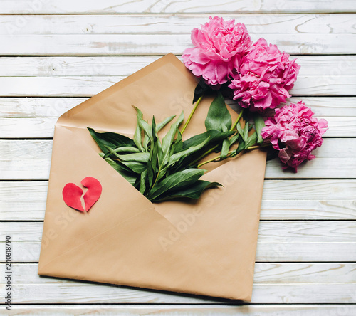 Fototapeta Naklejka Na Ścianę i Meble -  Three fade purple peonies lay in open brown kraft envelope containing. Copy space, marriage proposal. Valentine's Day concept. Symbol of unhappy love in the form of a broken heart.
