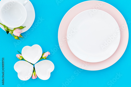 Elegant table setting with white and rose plates and floral decor on blue background top view mock up