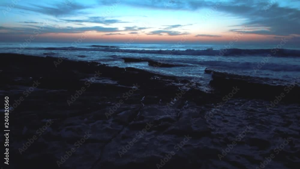 Gimbal shot of the beach in blue light with ocean waves hitting the rocks in the background. Shot after sunset. Gimbal shot of the beach in blue light with ocean waves hitting the rocks in the background. Shot after sunset.