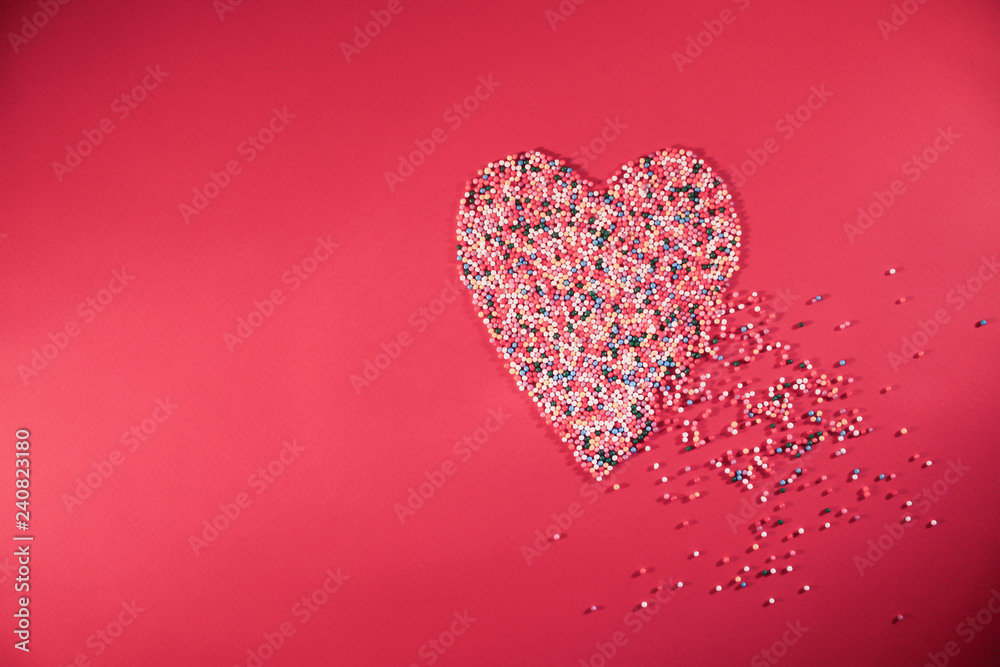 Heart made from confectionery colorful balls topping on pink background. Minimal Saint Valentine's Day concept. Flat lay. Top view.