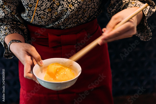 Bilde på lerret Woman wearing kimono is beating hen egg with chopsticks for dipping with sukiyaki beef