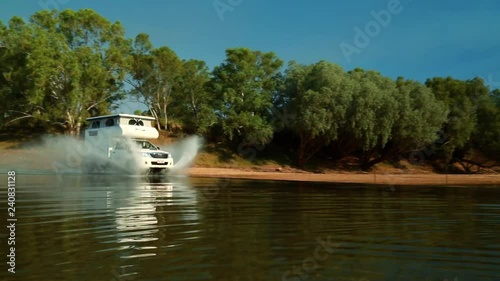 A caravan speeding through water in the outback splashing up big waves
