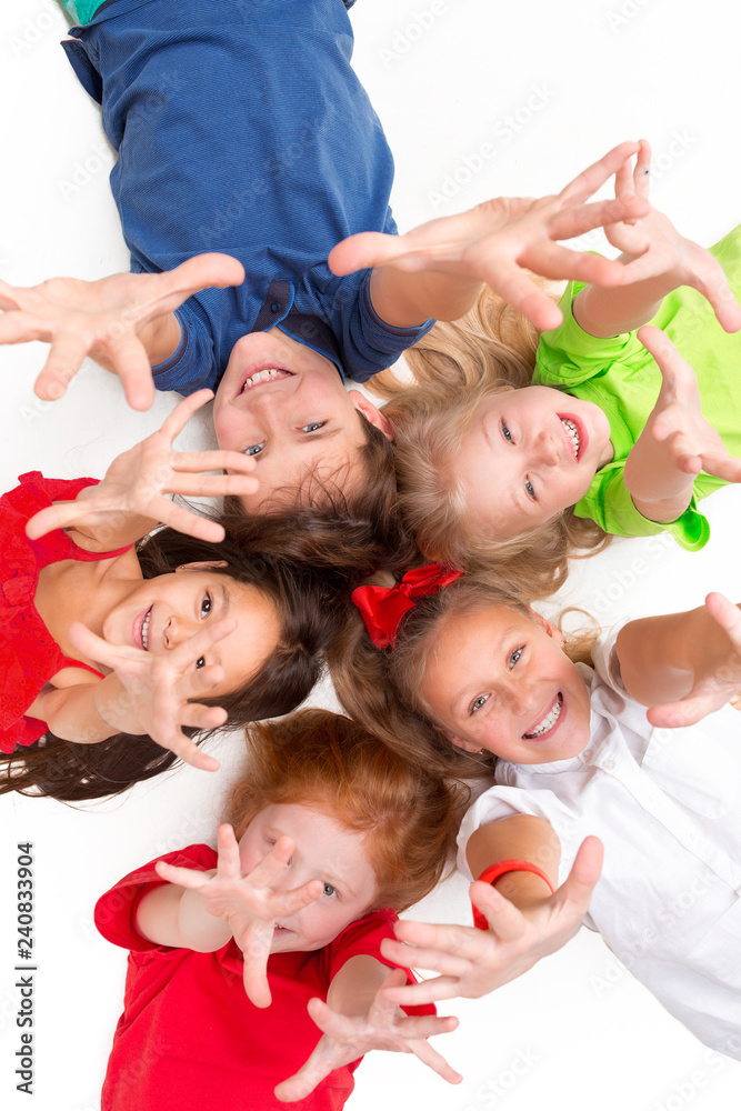 Close-up of happy children lying on floor in studio and looking up, isolated on white background, top view. Kids emotions and fashion concept