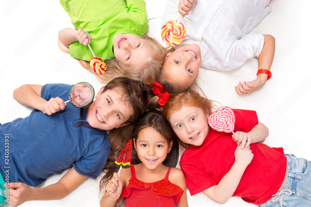 Close-up of happy children with candy lying on floor in studio and looking up, isolated on white background, top view. Kids emotions and fashion concept Close-up of happy children with candy lying on floor in studio and looking up, isolated on white background, top view. Kids emotions and fashion concept