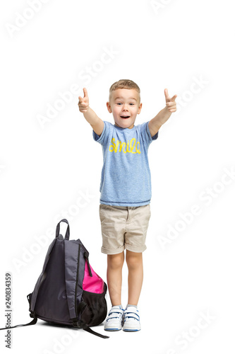 Full length portrait of cute little kid boy in stylish clothes looking at camera and smiling, standing against white studio wall. Kids fashion concept