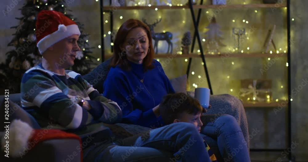 Medium shot of a happy family talking while watching television and changing channels at Christmas eve Medium shot of a happy family talking while watching television and changing channels at Christmas eve