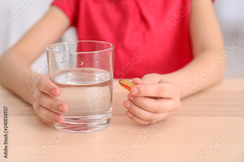 Little girl with pill and glass of water at table