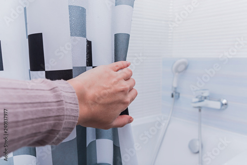 Hand holding shower curtain in white bathroom. photo