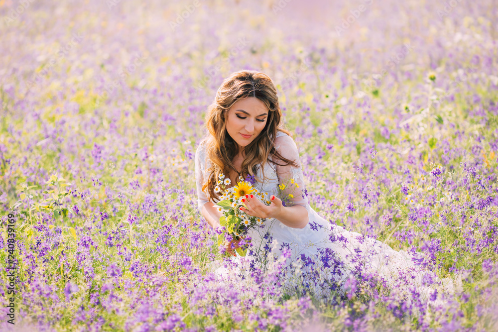 lovely sweet woman with closed eyes dressed in an elegant white dress with transparent sleeves sits in purple flowers with a natural field bouquet in her hands. atmospheric photo, gentle warm colors