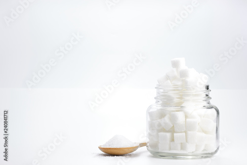 Cube granulated sugar in a glass jar and on wooden spoon for adding sweetness. - image