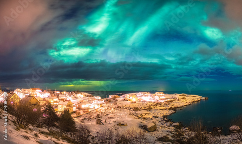 Norwegian village glowing on arctic coastline with northern lights