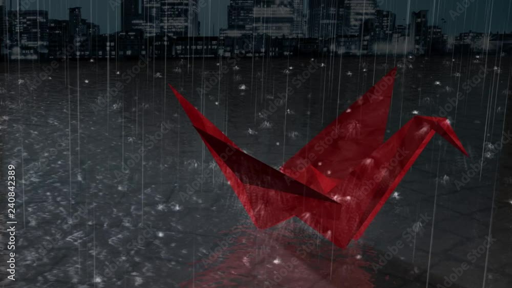Red Crane Rain features a city landscape background with rain falling down and splashing all around a origami crane made out of red paper that have been left outside.