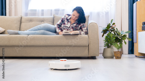 girl resting at home on the couch, while the robot vacuum cleaner. concept time for yourself. smart House. modern girl optimizes her time.