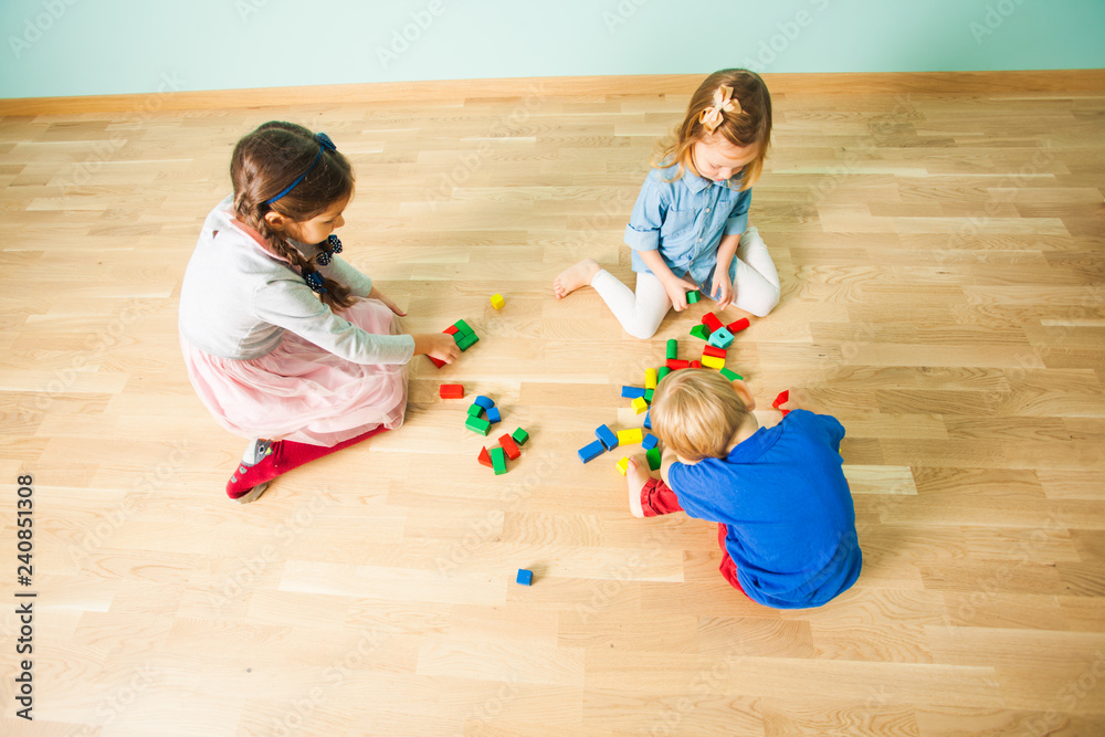 Fototapeta premium Three kids playing with wooden blocks in their room
