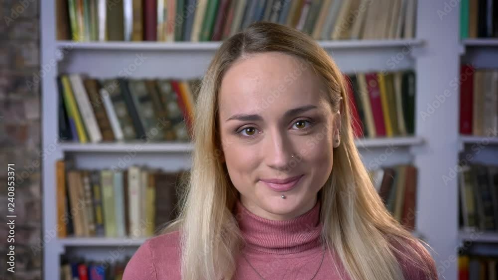 Close-up portrait of freaky caucasian young girl approvingly nodding into camera on book shelves background. Close-up portrait of freaky caucasian young girl approvingly nodding into camera on book shelves background.