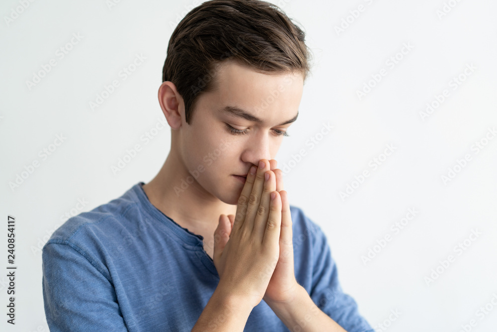 Pensive teenage guy asking for help. Closeup of serious young man in casual putting hands together in pray. Pray concept Pensive teenage guy asking for help. Closeup of serious young man in casual putting hands together in pray. Pray concept