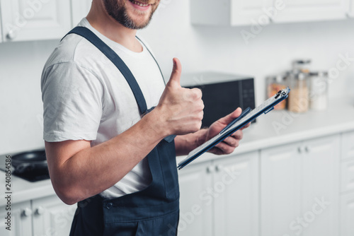 partial view of handyman holding clipboard and doing thumb up gesture in kitchen