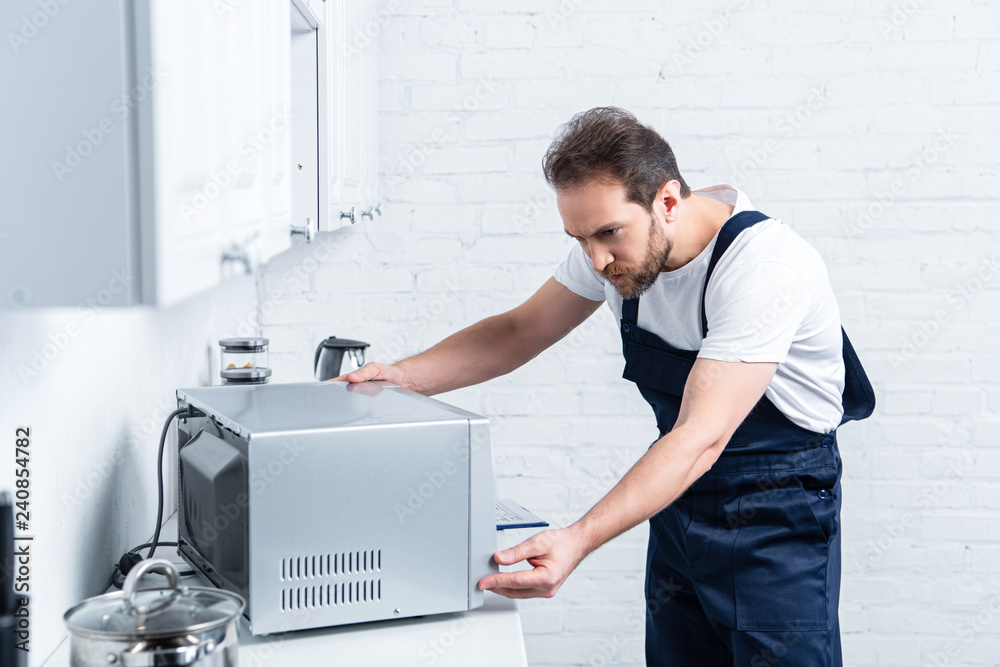 focused adult handyman repairing microwave oven in kitchen