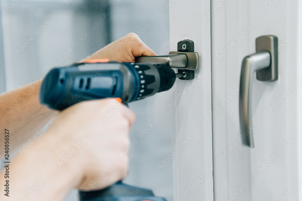 cropped shot of handyman fixing window handle by electric drill