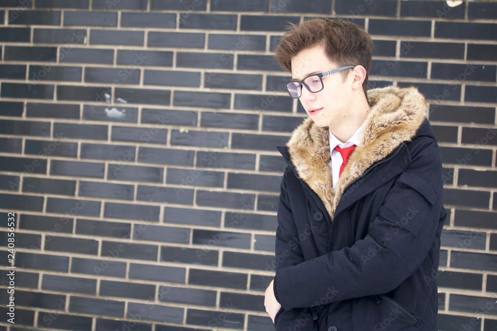 Portrait of a young man in a coat with a fur collar. On the background of a brick wall. Portrait of a young man in a coat with a fur collar. On the background of a brick wall.