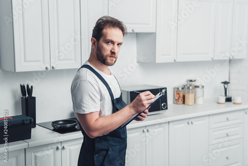 handsome adult bearded repairman with clipboard in kitchen