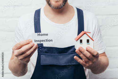 cropped image of male craftsman showing house model and card with lettering home inspection