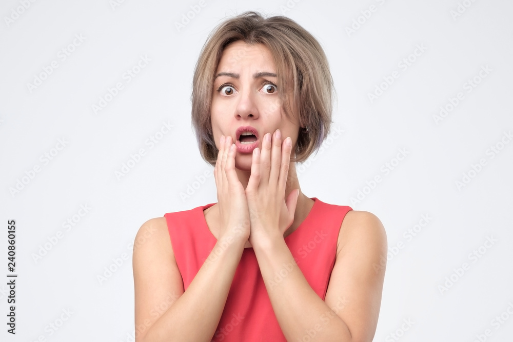 Surprised shocked female wearing red dress r, keeping her hand on cheek, opening mouth. Young girl with puzzled expression Surprised shocked female wearing red dress r, keeping her hand on cheek, opening mouth. Young girl with puzzled expression