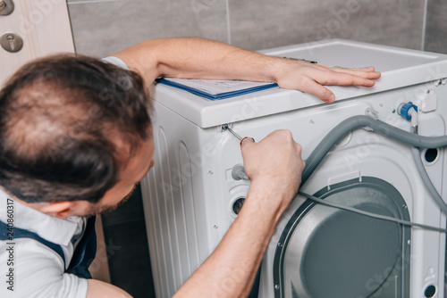 selective focus of male handyman repairing washing machine in bathroom