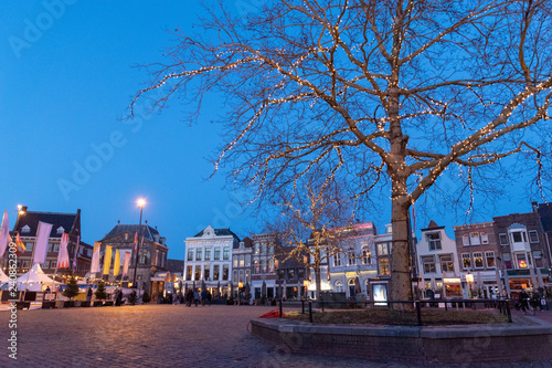 Fotografía Tree on a market square with ancient town houses with lights and a blue sky in the twilight