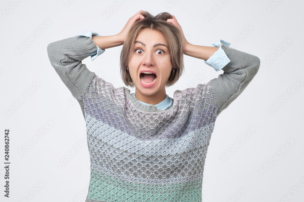 Shocked amazed young woman with hands on head standing and shouting over gray background Shocked amazed young woman with hands on head standing and shouting over gray background