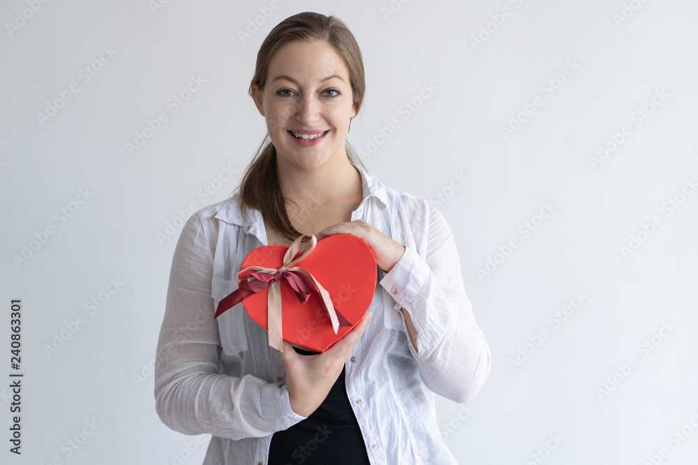 Happy pretty young woman holding heart shaped gift box. Girl looking at camera. Saint Valentines Day gift concept. Isolated front view on white background. Happy pretty young woman holding heart shaped gift box. Girl looking at camera. Saint Valentines Day gift concept. Isolated front view on white background.
