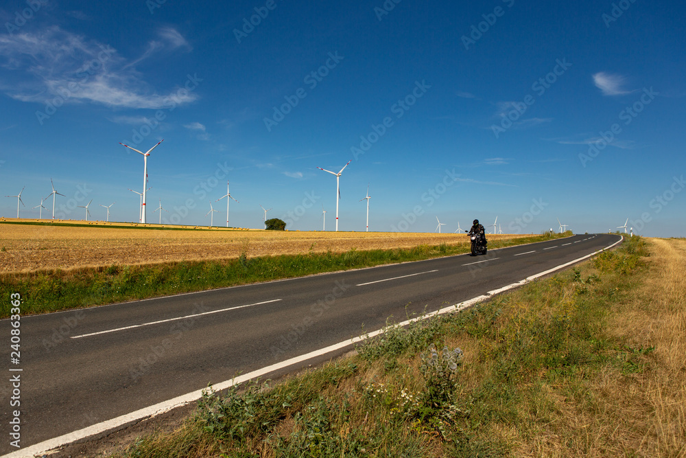 A motorcyclist in an agricultural landscape with wind turbines in the background