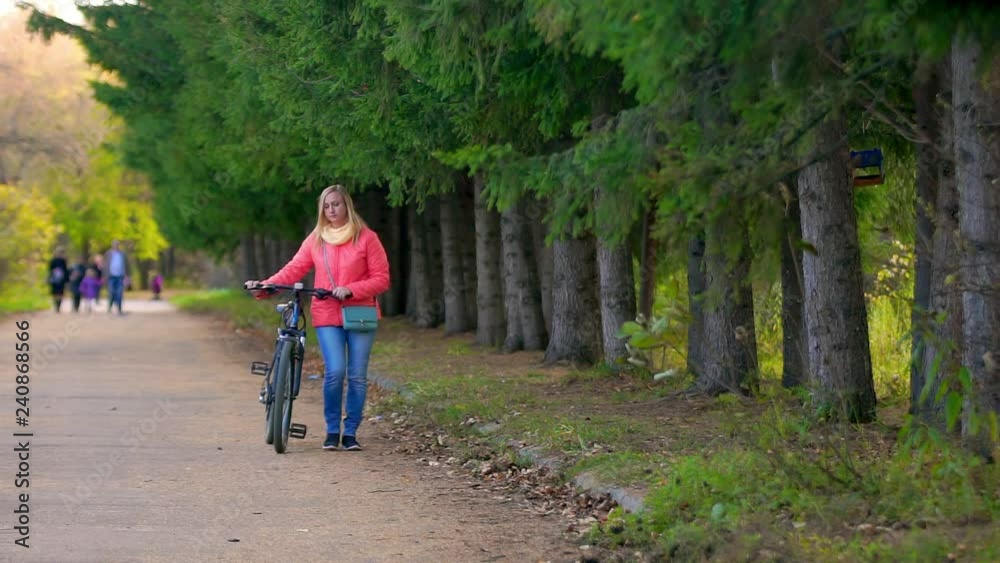 Woman walking with a Bicycle in the Park.She goes to the cameras in the distance Woman walking with a Bicycle in the Park.She goes to the cameras in the distance