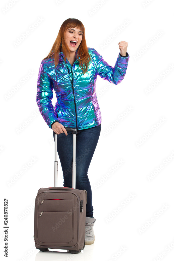 Excited Young Woman In Vibrant Down Jacket Is Standing With Trolley Bag And Shouting Excited Young Woman In Vibrant Down Jacket Is Standing With Trolley Bag And Shouting