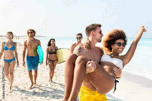 Friends walking on the beach, one man carrying his girlfriend