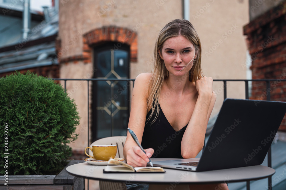 Portrait of young woman sitting on balcony with laptop taking notes Portrait of young woman sitting on balcony with laptop taking notes