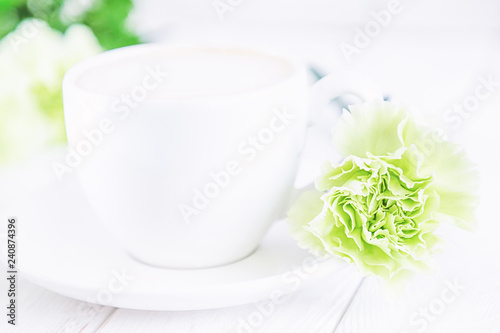 White cup of coffee cappuccino and green carnations flowers on a white background