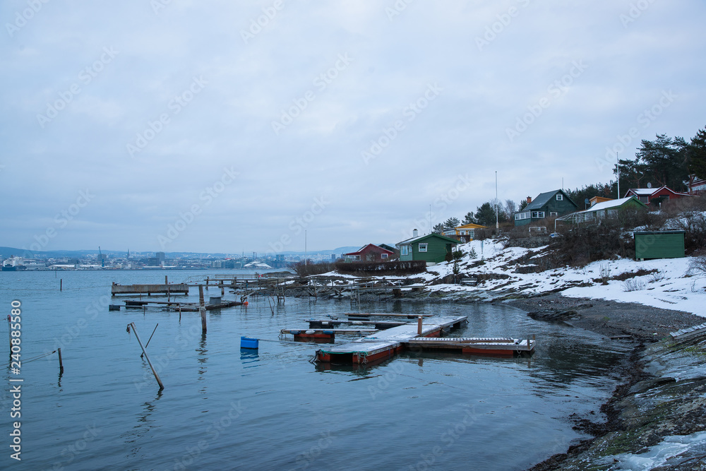 Fototapeta premium A pier for boats traveling between the Islands around Oslo Norway during the winter overlooking the sea and the Fjord covered by snow