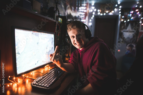 Portrait of an evil gamer gamer plays a game on a computer, looks at the evil eye of the camera and shows the middle finger. Wicked gamer shows middle finger