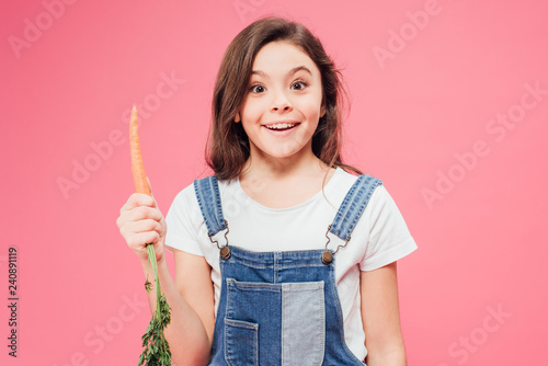 happy kid holding carrot isolated on pink