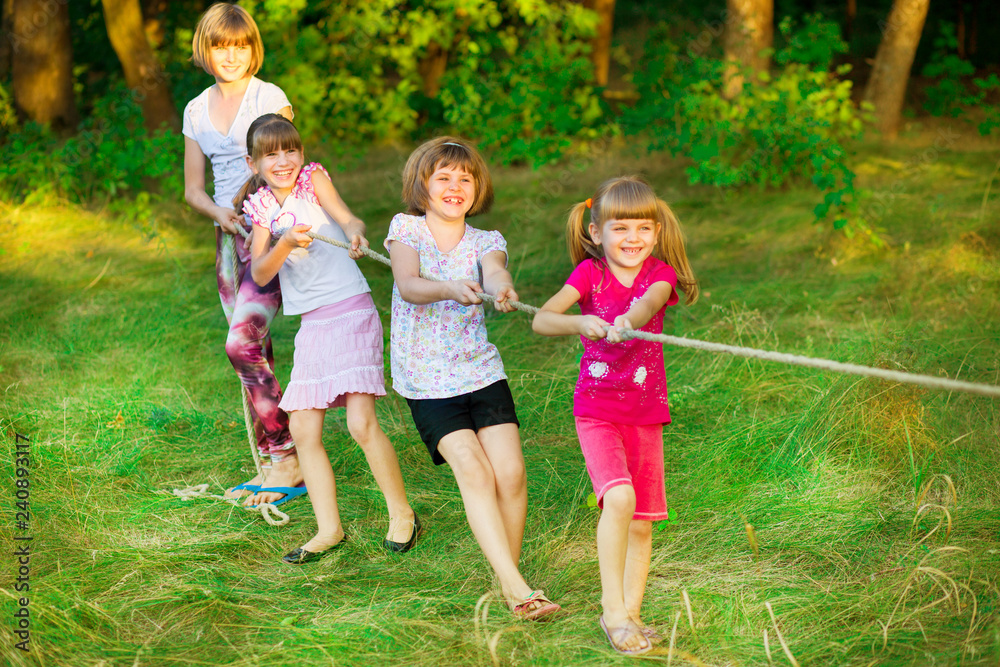 Fototapeta premium Group of happy children playing tug of war outside on grass. Kids pulling rope at park.