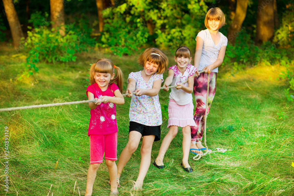 Fototapeta premium Group of happy children playing tug of war outside on grass. Kids pulling rope at park.