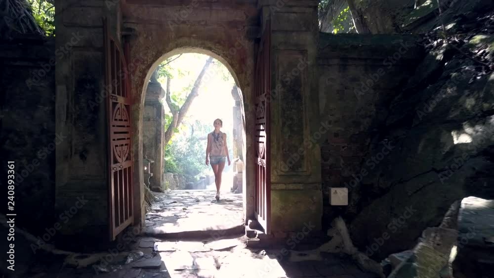 girl tourist enters cave through stone arch gate passes rocky walls ...