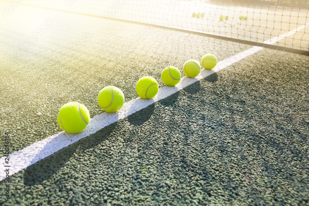 Tennis balls laid out in a row on a white line on a tennis court