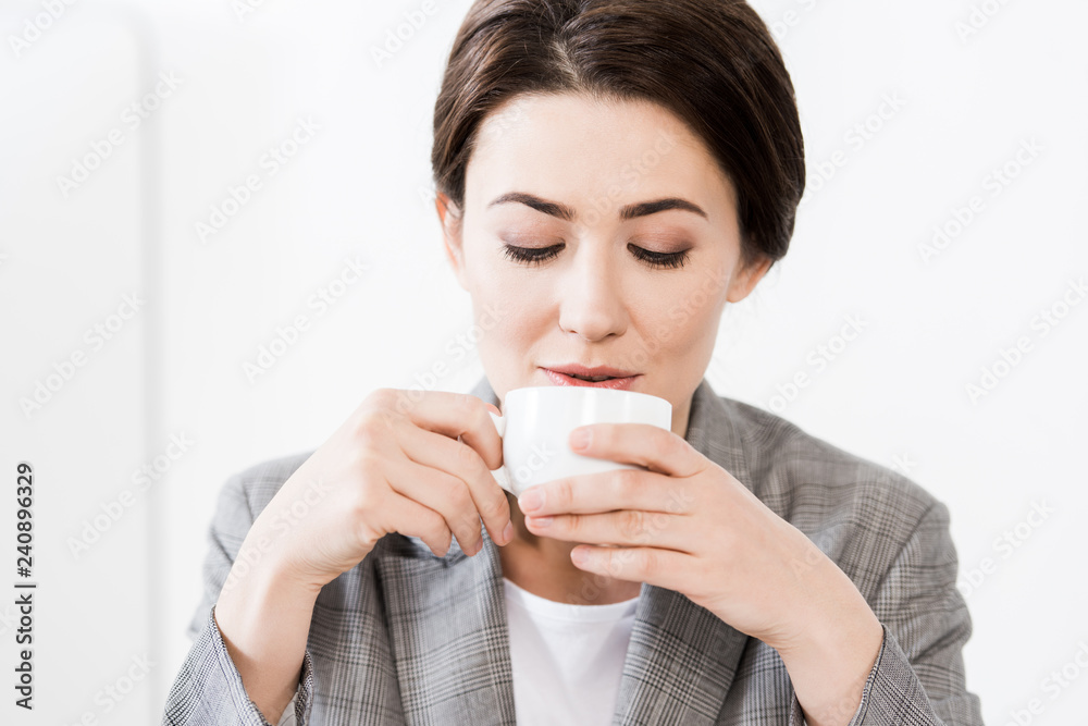portrait of attractive businesswoman in grey suit drinking coffee in office portrait of attractive businesswoman in grey suit drinking coffee in office