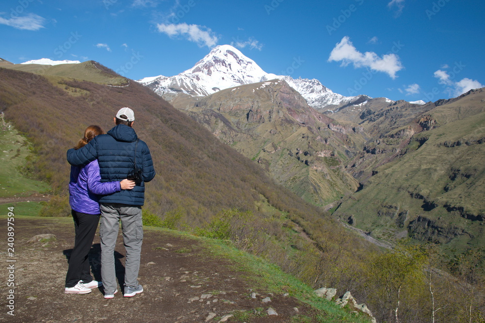 Man and woman stand embracing and look at the snow-capped peak