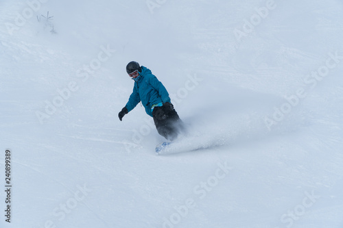 Bottom view of freeride snowboarder sliding down the snowy slope against the clear blue sky